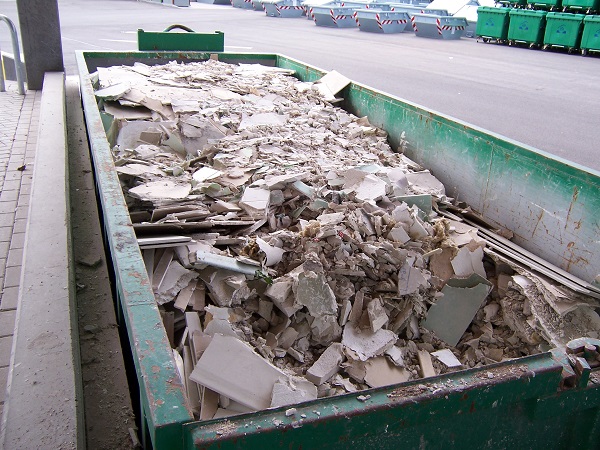 Blick auf einen mit Bauschutt gefüllten Container; Im Hintergrund sind weitere Abfalltonnen zu sehen.