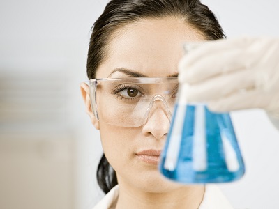 Eine Laborantin sieht mit geübten Blick auf eine Flüssigkeit in einem Reagenzglas, welches sie vor Ihre Augen hält.