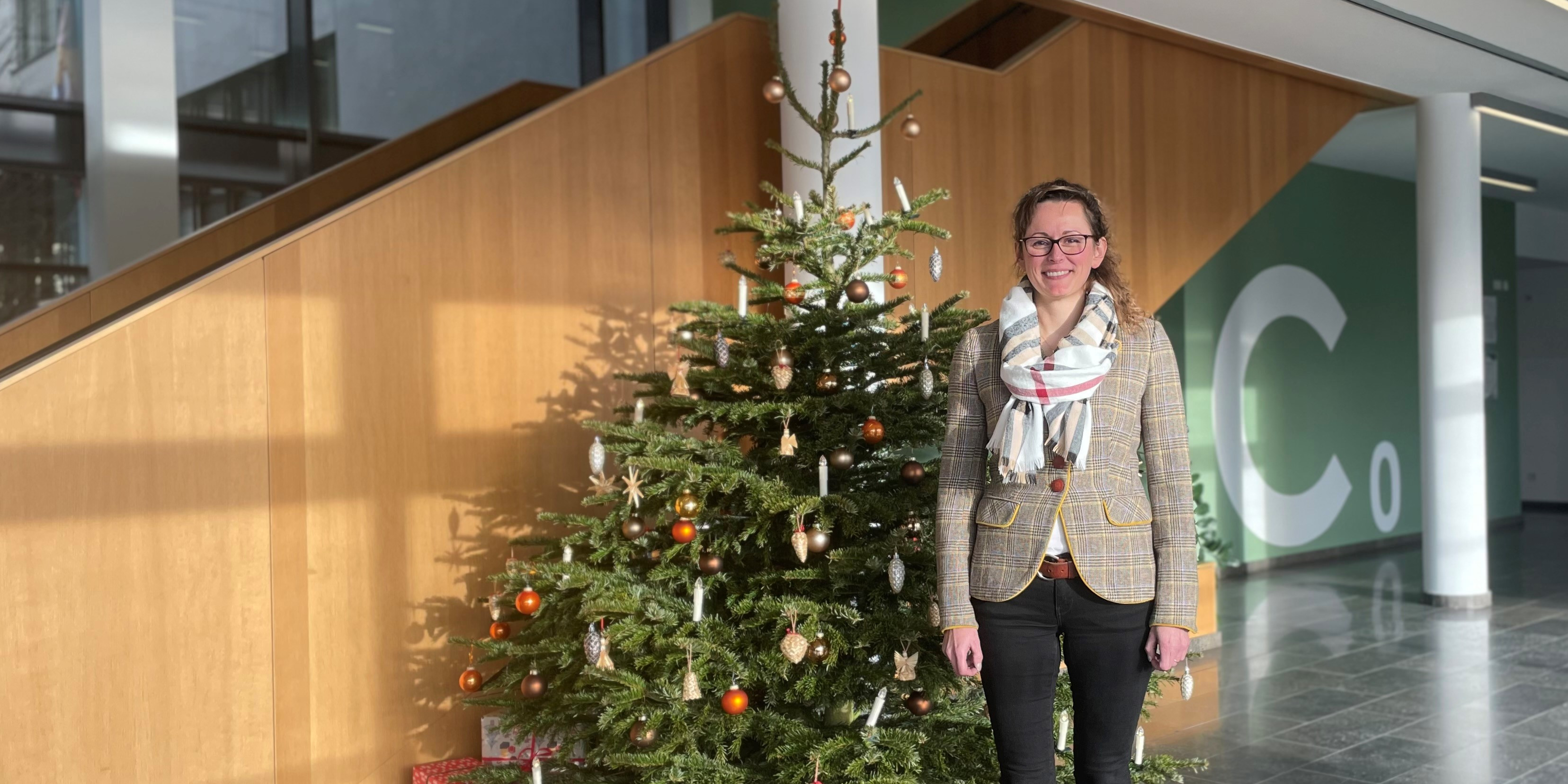 Ministerin Hanke Mittestädt stht neben einem geschmückten Weihnachtsbaum im Foyer des Ministeriums.